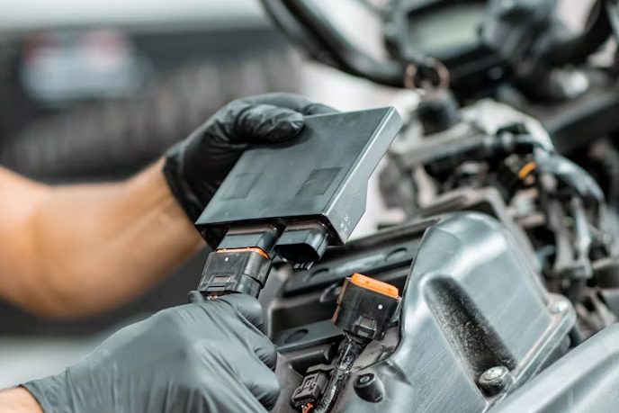 A gloved hand holding a component clear of the frame of a partly stripped motorcycle on a workbench