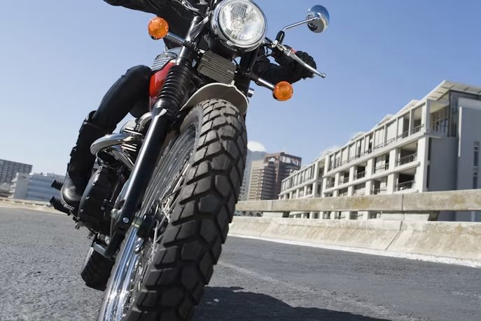 A scrambler style motorcycle parked on a concrete apron in front of a plain concrete building, photographed from a low angle