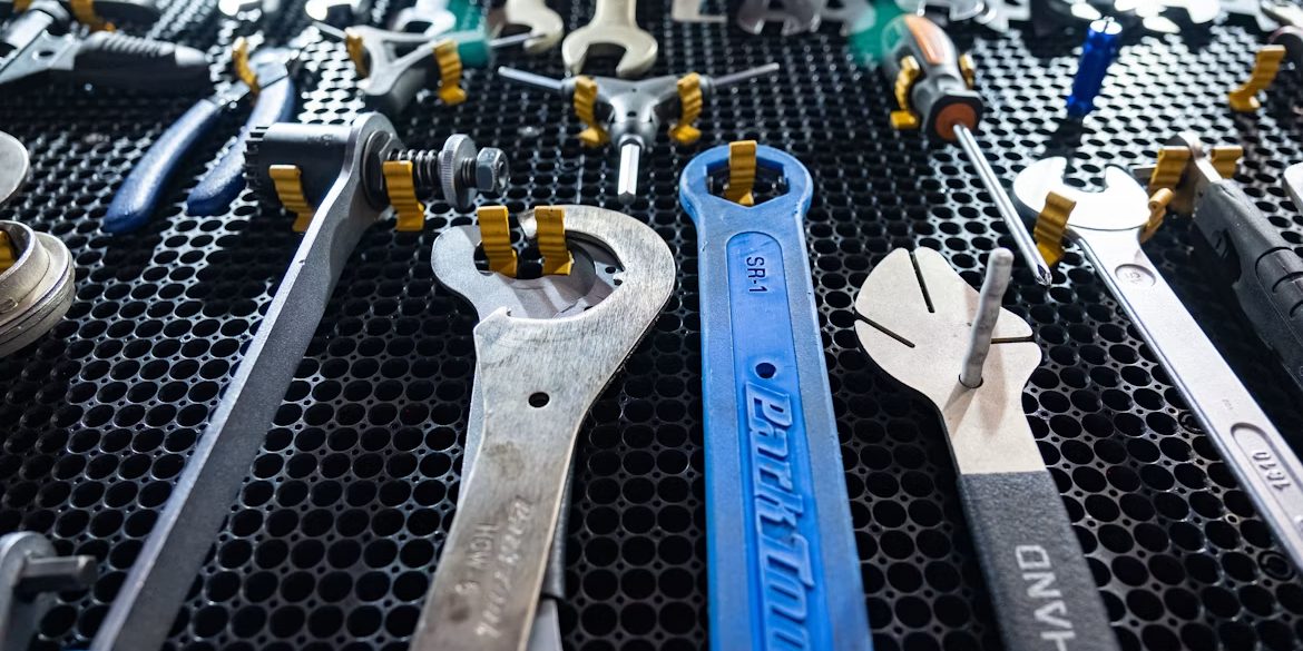 Combination spanners and hand tools laid out in order across a black rubber bench mat