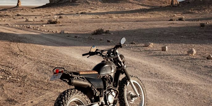 A dirt motorcycle standing alone on a track in open dry country, with rock formations on the skyline and no other vehicle in sight