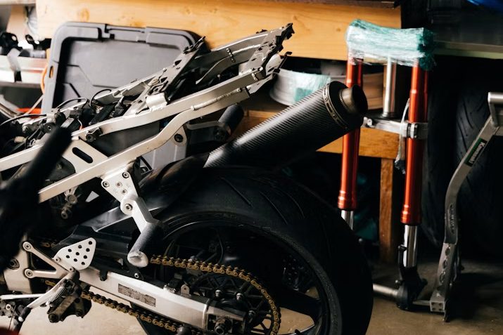 A partly stripped motorcycle in a home garage surrounded by tool cases, a workbench and stacked parts
