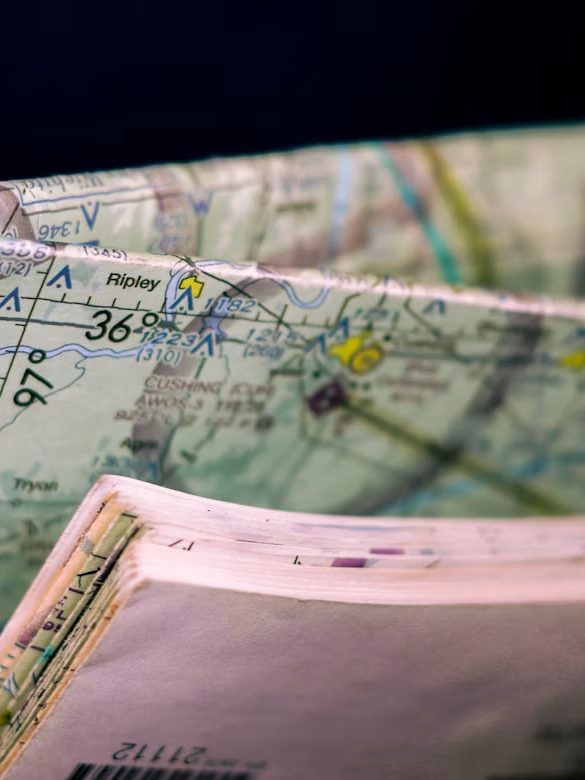 Folded paper maps overlapping on a table, marked up by hand with drawn lines and highlighted routes