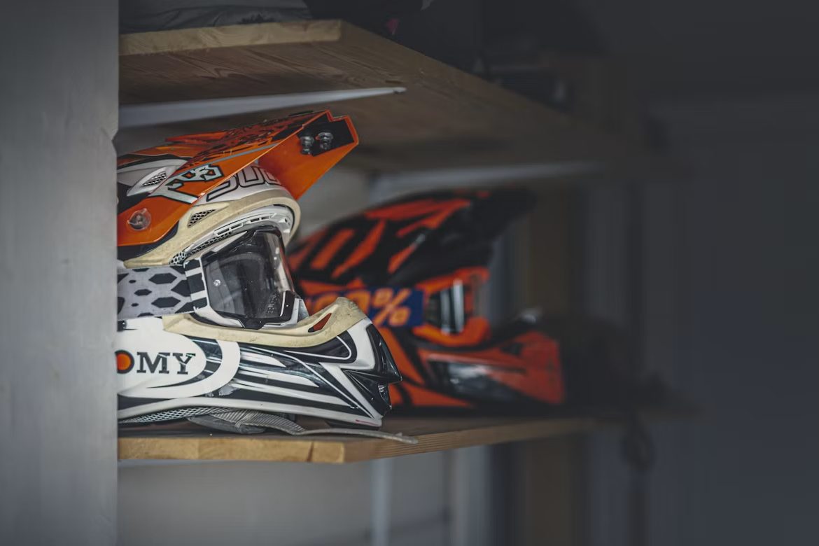 A motocross helmet with orange and white graphics resting on a shelf in soft light