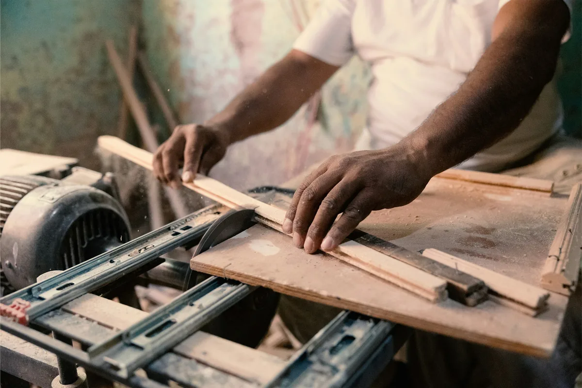 A craft worker’s hands guiding a plank of wood through a workshop cutting machine