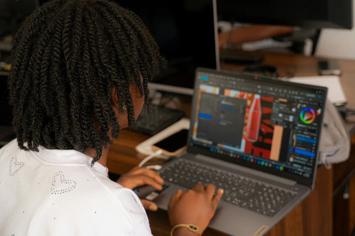 A young woman with braided hair working on a laptop at a wooden desk
